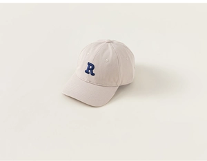 Detail of beige cotton baseball cap featuring a navy blue 3D embroidered letter R