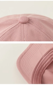 Detailed close-up of pink cotton baseball cap crown button and visor stitching lines
