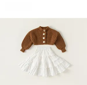Detailed view of girls brown knit cardigan with vintage gold buttons and white lace skirt