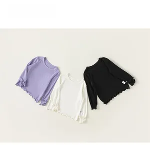 Dettaglio flat-lay di maglie a maniche lunghe per bambina in viola, bianco e nero con volant