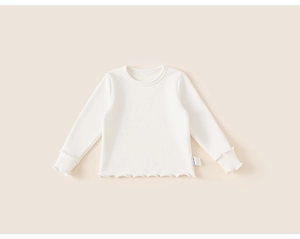 Dettaglio del tessuto in cotone a coste crema con delicati bordi a balze sulla maglia bimba