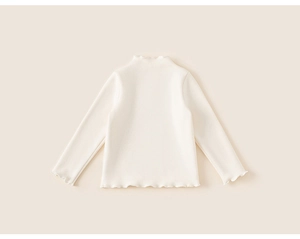 Detail of sweet off-white kids long sleeve top with ruffle edges and soft cotton texture