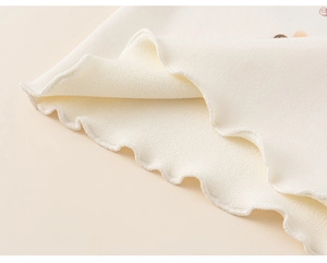 Detail view of the cream ruffled hem and warm fleece lining on a girls thermal long sleeve top