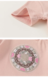 Detailed close-up of pink knit fabric showing traditional embroidery and ribbed sleeve cuffs