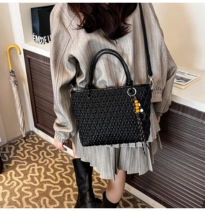 Detail of black woven bucket bag showing braided texture and beaded charm accessory