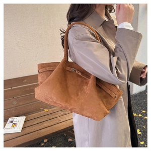 Detail view of brown suede tote bag with metal twist lock and strap on autumn background