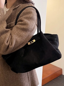 Minimalist black suede tote bag with gold metal buckle shown on a model in a brown blazer