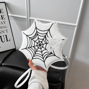 Detail einer weißen Umhängetasche in Spinnennetzform mit Stickerei und Spinnenanhänger