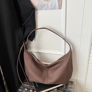 Detail of a brown lychee pattern leather crescent bag with a silver zipper on a suitcase