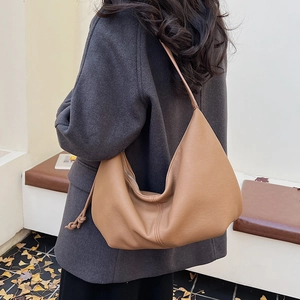 Detailed side view of camel moon bag with knot accents on a model in autumn scenery