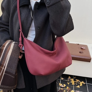 Detail of burgundy leather crossbody bag with knot strap on a stylish autumn coat
