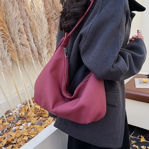 Detailed side view of a burgundy leather hobo bag worn by a model in a fall setting
