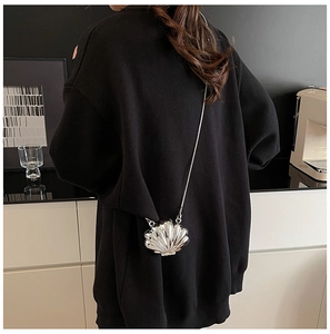 Detail of silver shell-shaped mini chain bag worn by a model in casual black hoodie