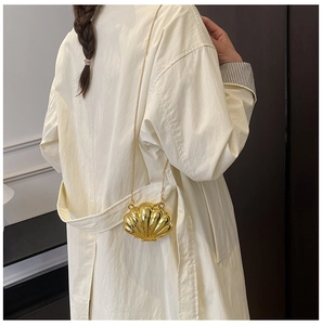 Close-up of a mini gold shell chain bag worn over a beige coat for a stylish look
