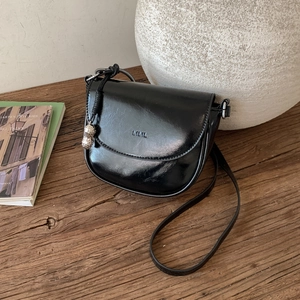 Detalle de bolso de silla negro brillante con logo grabado y colgante de maní metálico