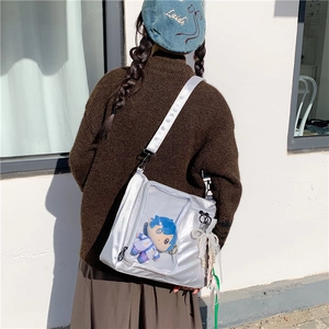 Silver ita bag featuring a transparent display window with a plush doll and lace charms