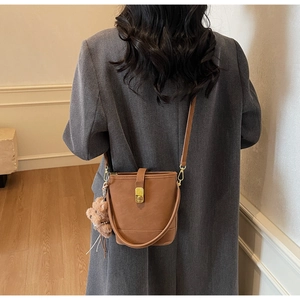 Détail d'un sac seau en cuir marron avec fermoir doré et breloque ours sur un mannequin