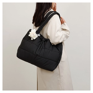 Detail of a large black quilted puffer tote bag with drawstring and plush charm