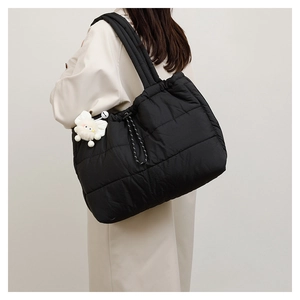 Detail view of large black quilted puffer tote bag with a white plush bow pendant charm