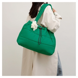 Detail view of large green quilted puffer tote bag with black drawstring and plush charm
