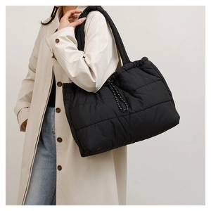 Detail of black quilted puffer tote bag with rope drawstring on beige trench coat
