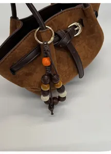 Dettaglio di un ciondolo colorato con perle di legno su una borsa tote in pelle scamosciata