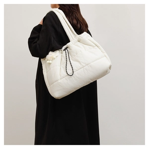 Detail of quilted puffer tote bag in cream white featuring adjustable drawstrings and plush ball