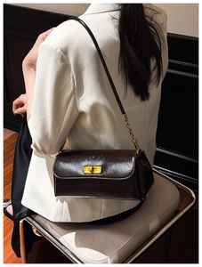 Deep brown glossy leather underarm bag with gold clasp shown on a model in a white blazer