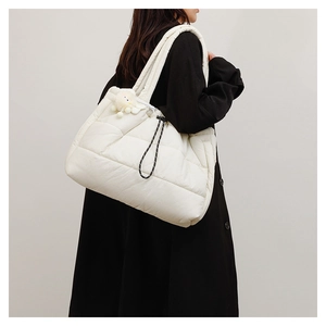 Detail of white quilted puffer tote bag with plush keychain worn on black coat