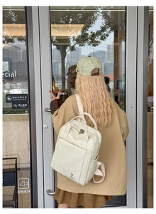 Outdoor shot of a cream white business casual backpack with a cute cartoon logo on the back