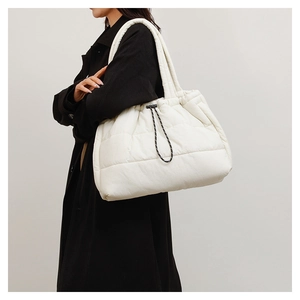 Model wearing a large white quilted puffer tote bag with decorative drawstrings