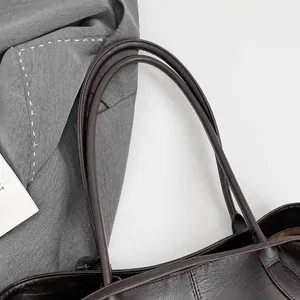 Close-up of durable round handles and stitching details on dark textured leather tote