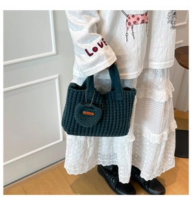 Detailed texture of thick dark green knit handbag with heart-shaped handmade pendant