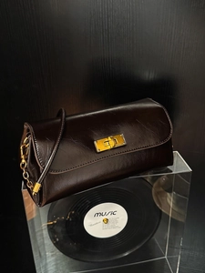Brown oil wax leather shoulder bag with gold metal lock and chain strap on record stand