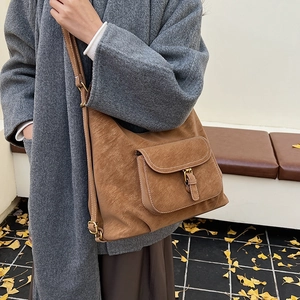 Detailed view of brown suede shoulder bag with gold metal buckle on autumn leaves