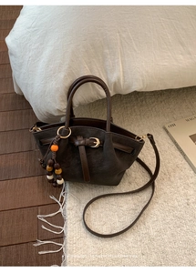 Dettaglio borsa tote marrone scuro opaco con ciondolo etnico su morbido tappeto bianco