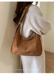 Sac hobo en daim minimaliste et rétro porté à l'épaule avec un long manteau chic