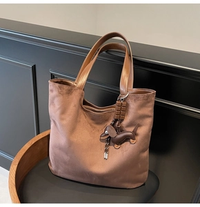 Close-up of brown suede tote bag with dachshund pendant and fine leather handle details