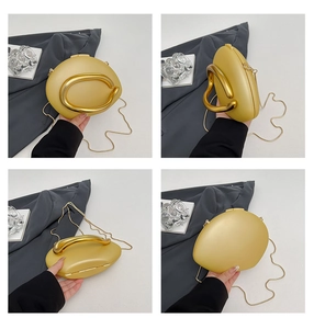 Detail van gouden avondtas met een grof metalen handvat en fijne metalen ketting