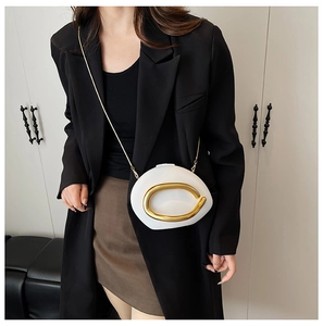 Chique witte ovale crossbodytas met gouden ring handvat gedragen bij een zwarte blazer