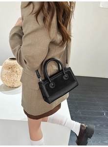 Detail of a matte black leather square bag showing spherical handle joints and shoulder strap