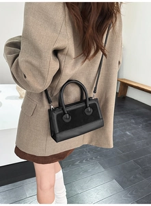 Detail of a black minimalist square bag with mixed textures on a model's shoulder