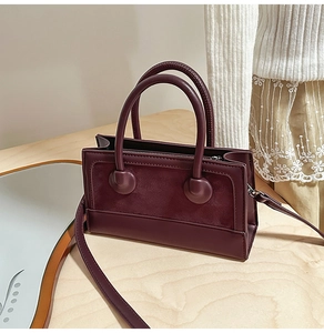 Detail view of burgundy leather and suede paneled small square bag with top handles