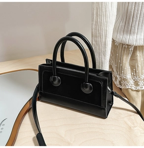Detail view of a black matte leather rectangular mini bag on a natural wooden surface