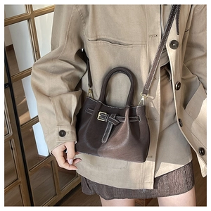 Detail view of dark brown leather handbag with contrast stitching and strap on a model