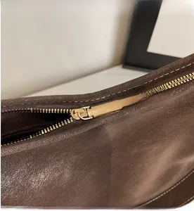 Vue macro d'un sac en cuir marron foncé avec fermeture éclair dorée et coutures blanches