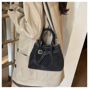 Detail of black suede tote bag with contrast stitching and golden hardware buckle