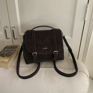 Dettaglio di uno zaino vintage marrone scuro con fibbie argentate su un divano crema