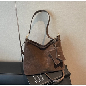 Détail du sac hobo en daim café noir avec logo doré posé sur un livre de design
