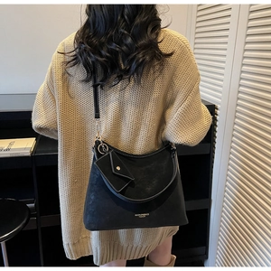 Détail du sac demi-lune en daim noir avec coutures contrastées et pendentif enveloppe